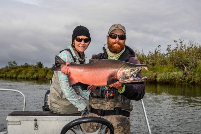 customer and guide hold up a bright red Coho salmon from the goodnews river