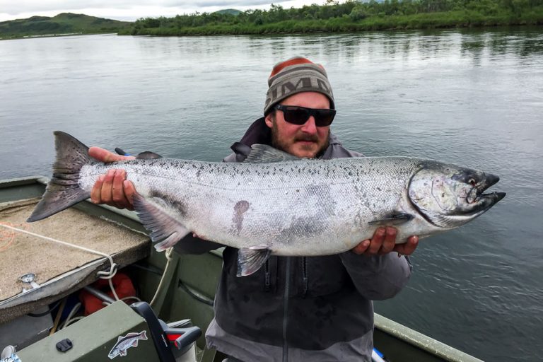 Customer in the boat holding up his prize a big Chinook salmon