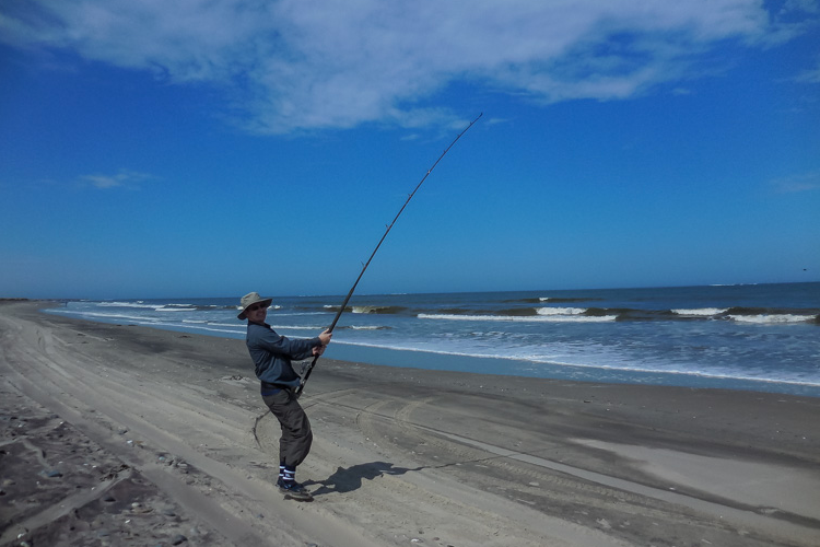 Angler With Rod Bent On The Beach