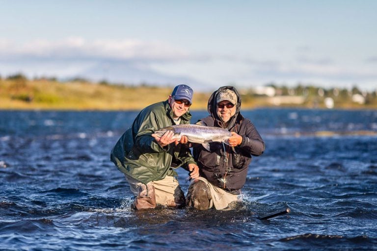 Customer and guide standing in the west ranga river on a windy day holding up for the camera thier atlantic salmon.