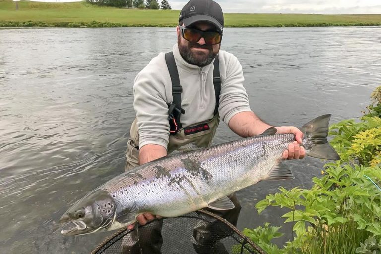 A customer holding a big Atlantic Salmon from the river which has scratch marks on the side of the fish.